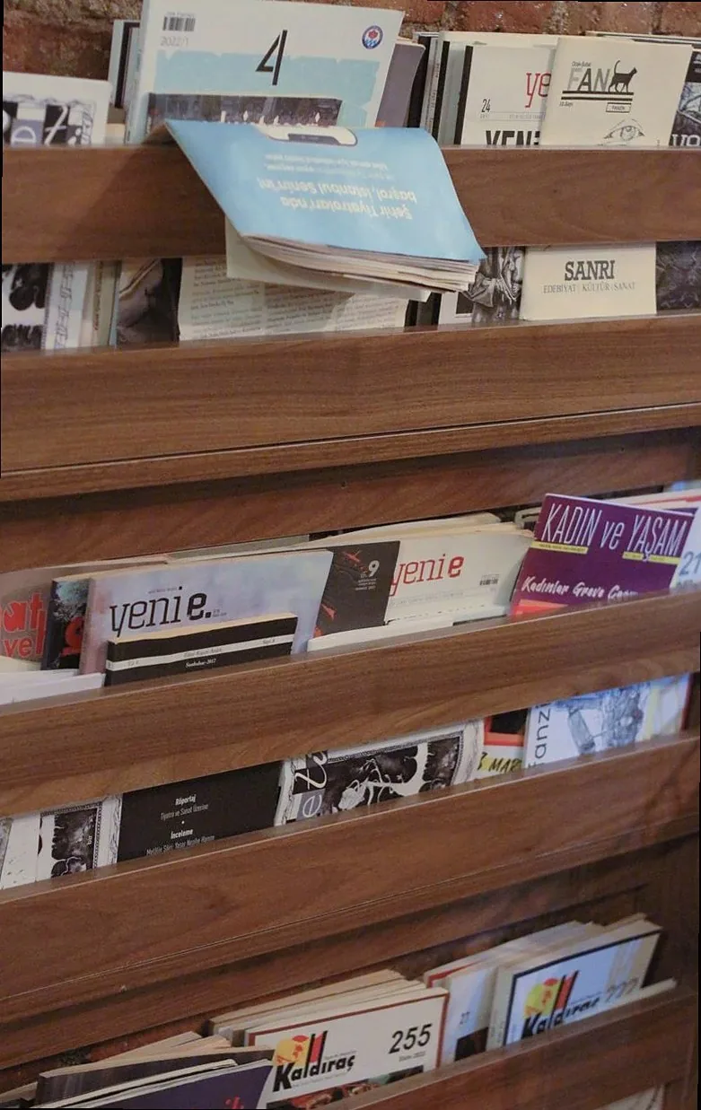 Wooden magazine rack filled with various journals in a cozy bookstore setting.