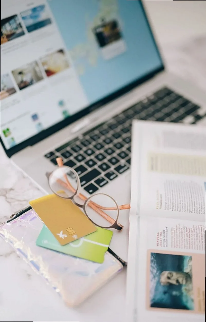 An open laptop with eyeglasses, credit cards, and a magazine on a work desk.